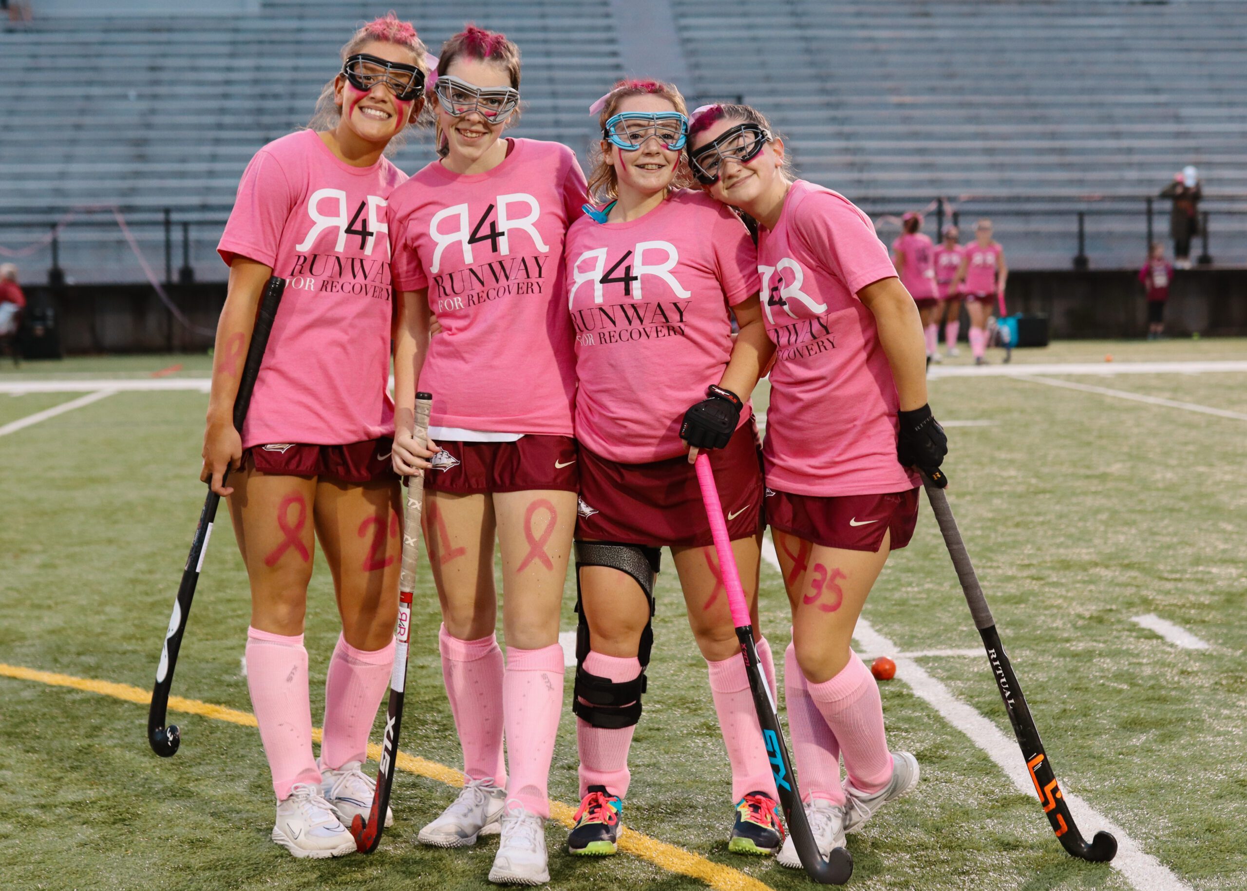 Four high school field hockey players posing in pink gear for a breast cancer awareness game.