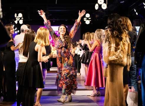 smiling woman in print dress on fashion runway with arms raised
